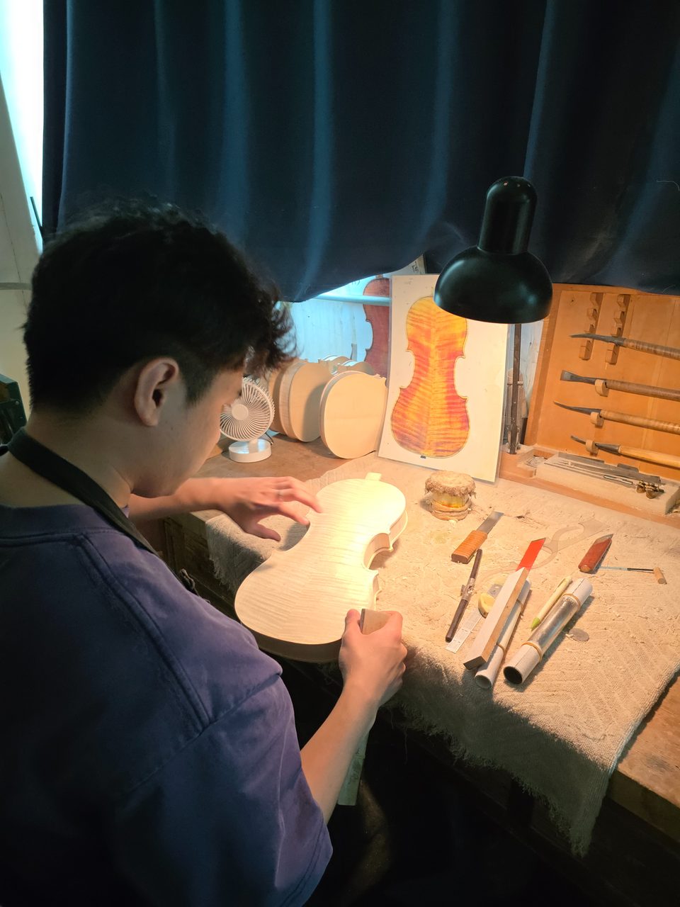 Yufan Chen carving the top plate of a violin at his workshop bench